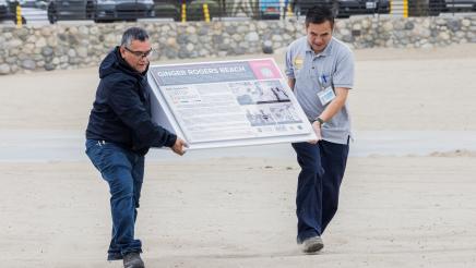 Educational signage signifying the history of Ginger Rogers Beach is carried toward the lifeguard towers