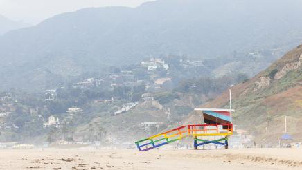 A newly painted lifeguard tower on Ginger Rogers Beach, with a green hillside covered with homes in the background