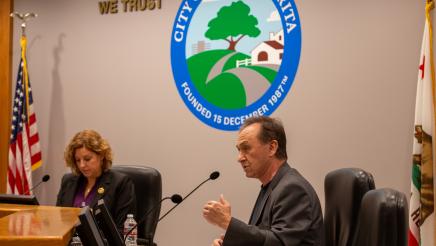 Asm. Zbur speaking and holding one hand up, with City of Santa Clarita logo in background