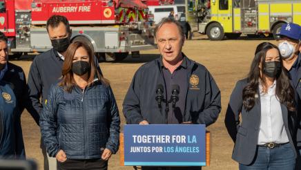 Asm. Zbur at podium, speaking, with fire engines in background