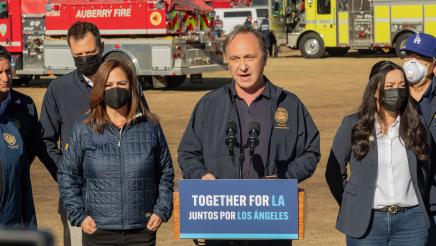 Asm. Zbur at podium, speaking, with fire engines in background