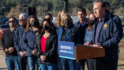 Asm. Zbur at podium, speaking, as other assemblymembers stand in support