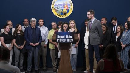 Guest speaker at podium, speaking as legislators and activists listen on